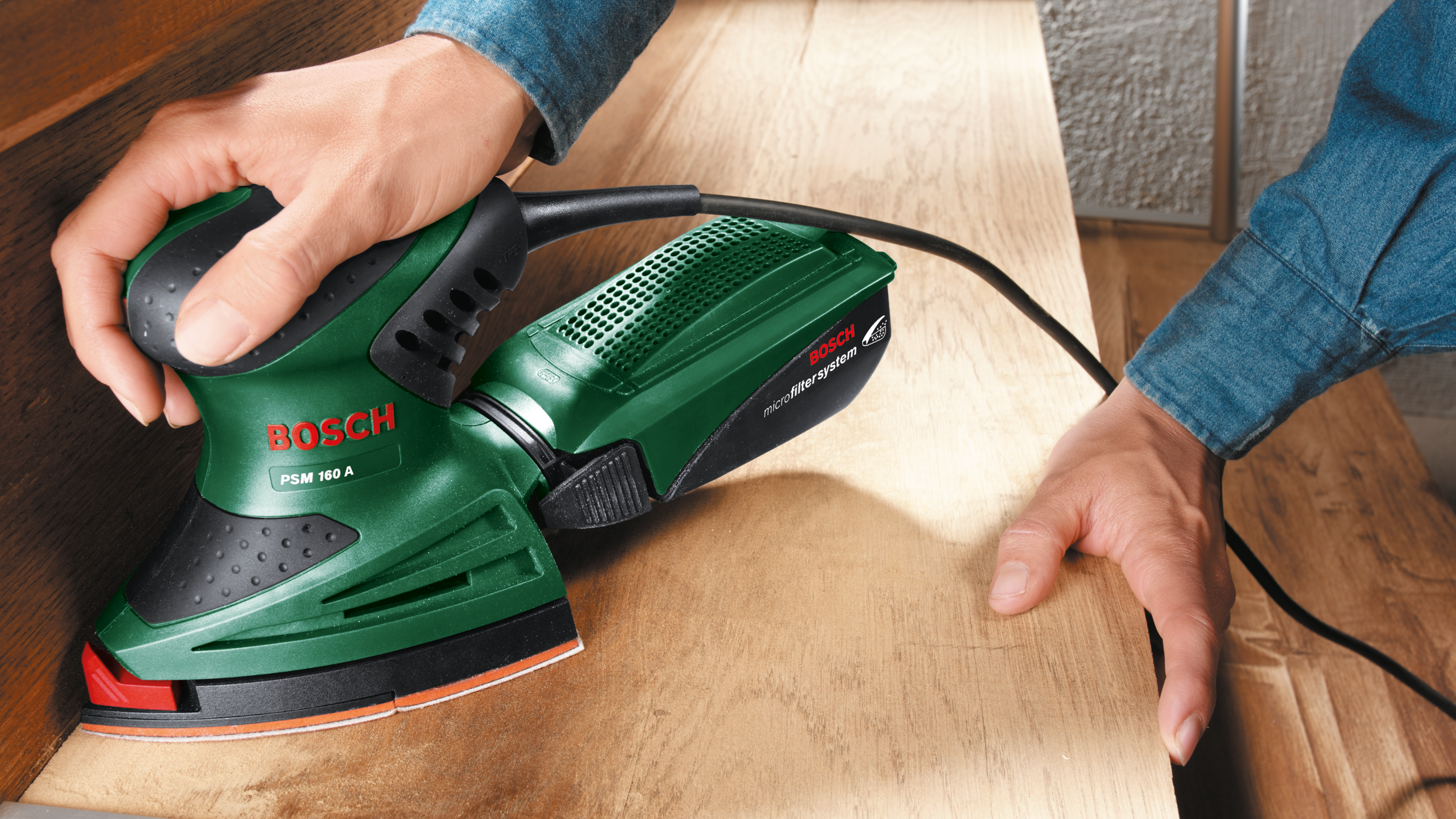 Lijadora Bosch verde es usada por manos sobre madera.