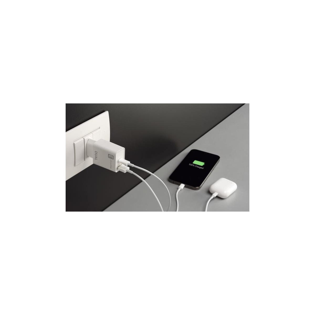 A white dual USB charger plugs into a wall, charging a phone and earbuds.