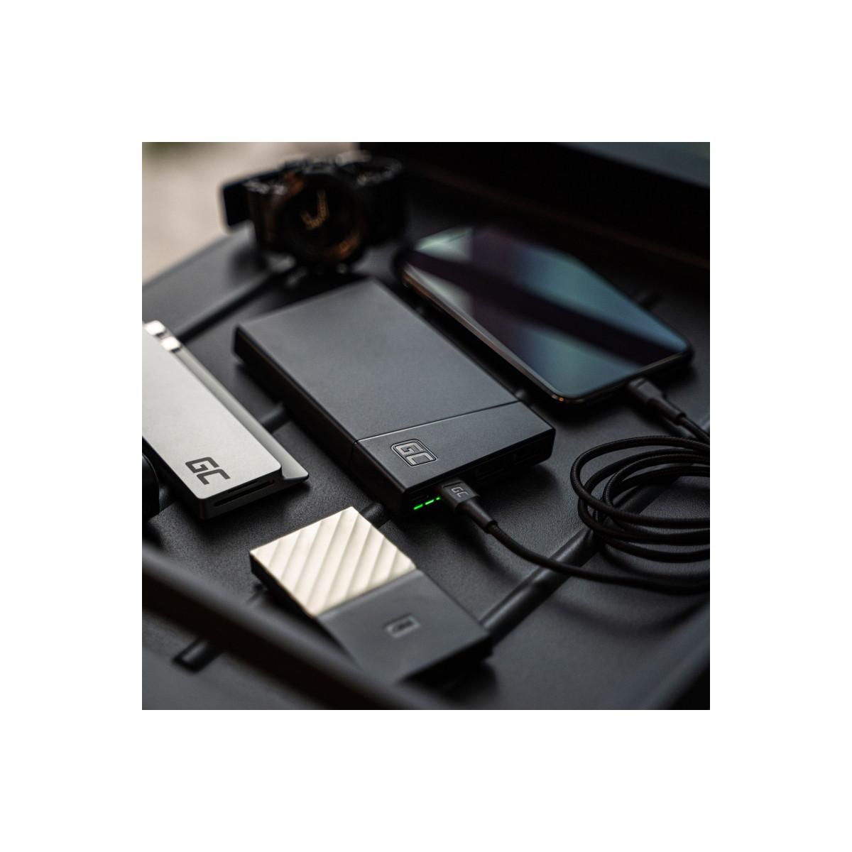 Un power bank nero carica uno smartphone. Accanto ci sono un power bank argentato e un piccolo SSD.