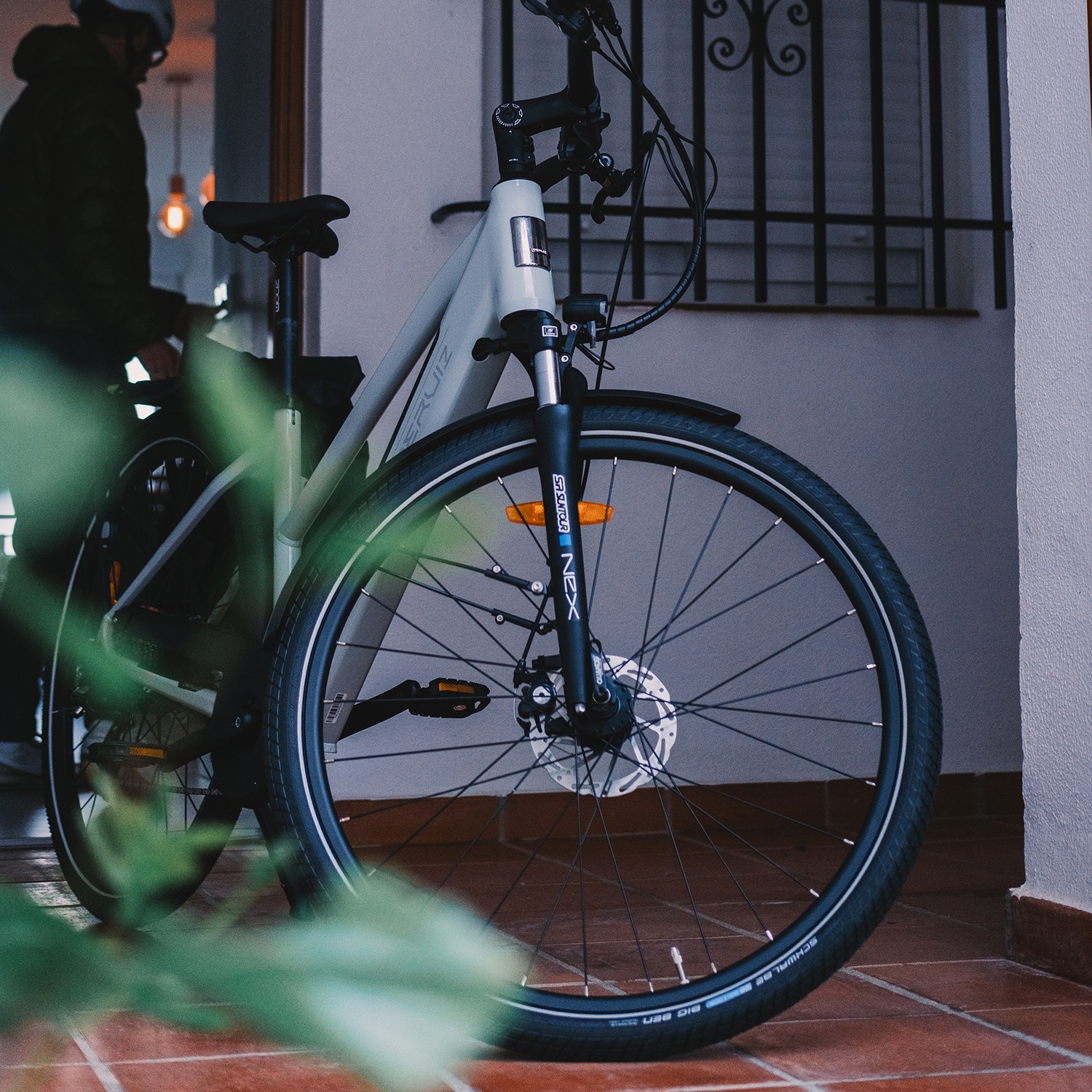 Ein hellgraues Fahrrad mit schwarzen Reifen steht drinnen, eine Person in dunkler Jacke ist teilweise sichtbar.