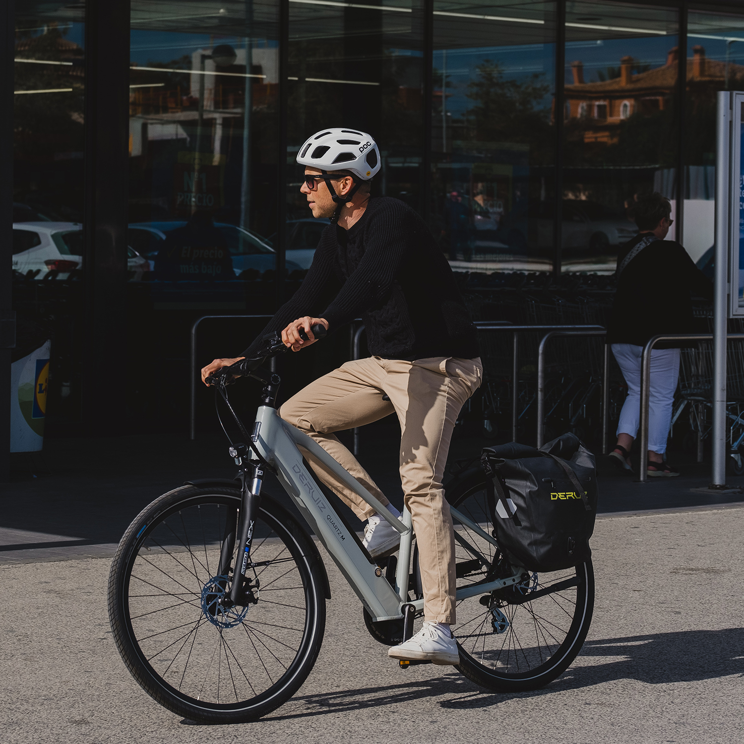 Mann fährt Fahrrad vor Geschäft. Er trägt Helm und Sonnenbrille.