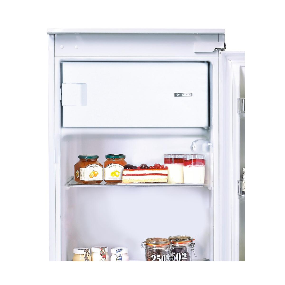 Un refrigerador abierto con compartimento congelador, pastel, vasos y tarros.