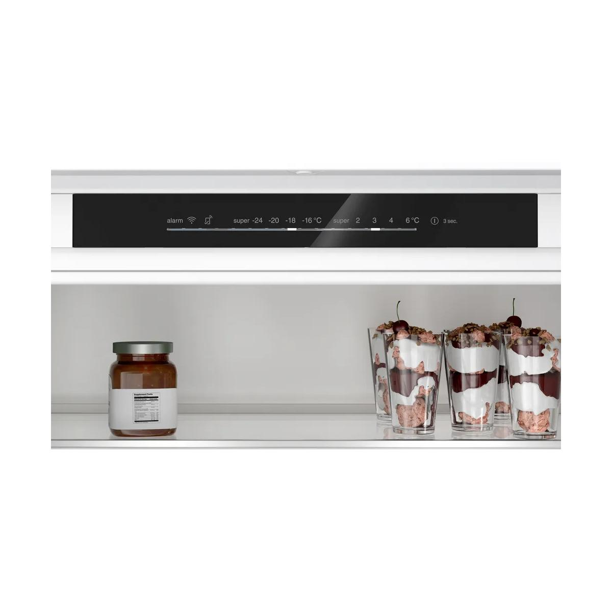 Ein Glas Marmelade und vier Desserts in Gläsern auf einem Kühlschrankregal.