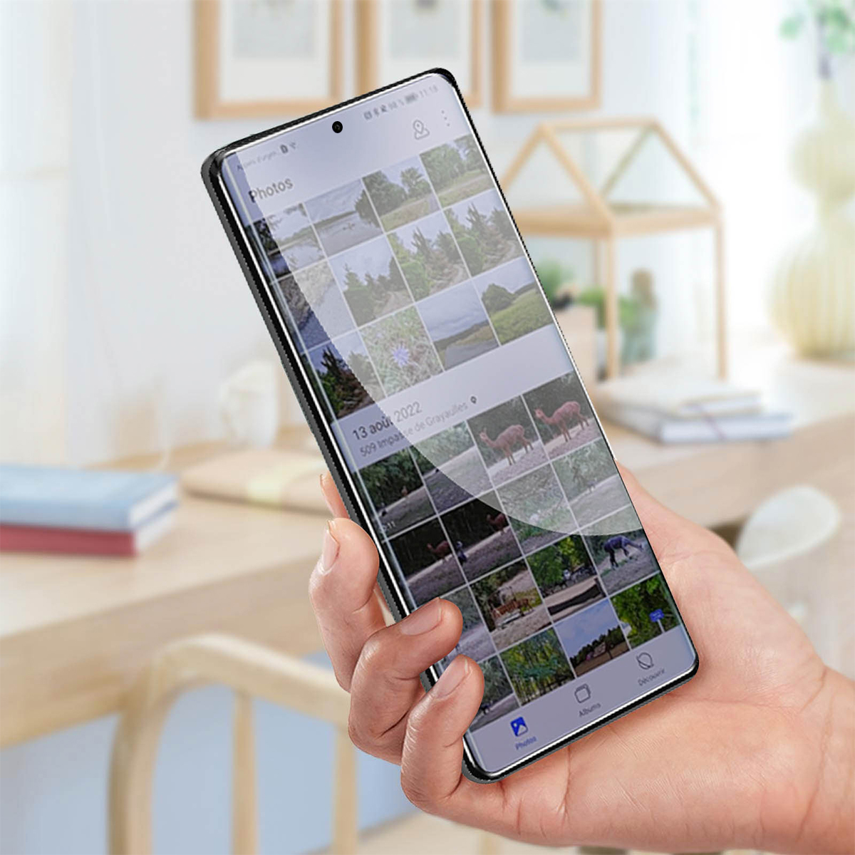 Una mano tiene uno smartphone che mostra una griglia di foto, con animali e paesaggi.