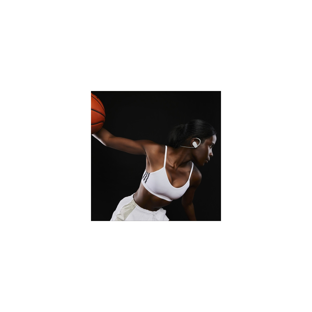 Una donna in abbigliamento sportivo tiene un pallone da basket, sfondo scuro.
