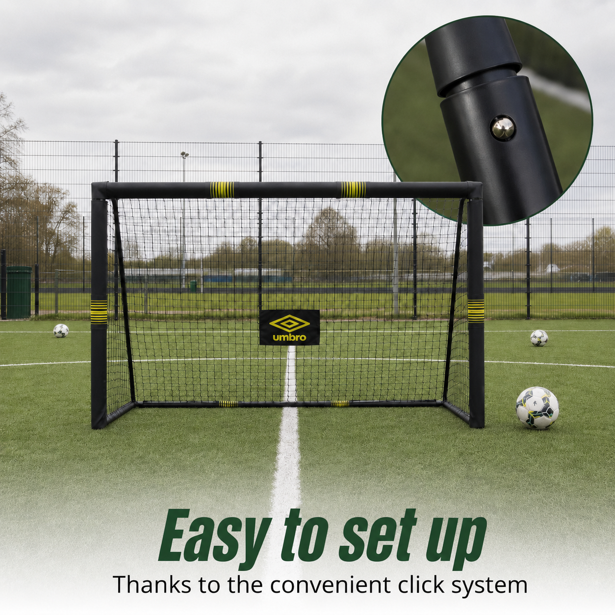 A black soccer goal with a net stands on artificial turf. Three soccer balls are nearby.