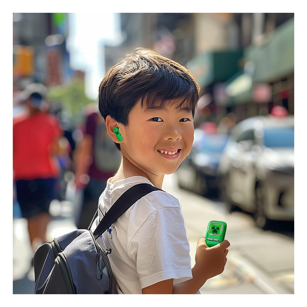 A boy smiles at the camera, wearing Minecraft earbuds and holding a controller.