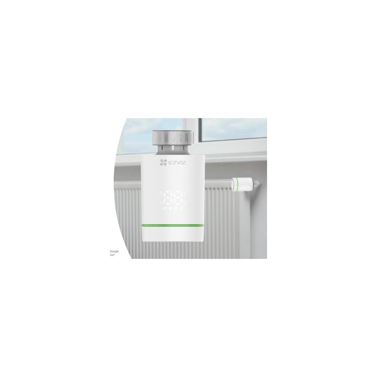 A white thermostat with a digital display is mounted on a radiator.