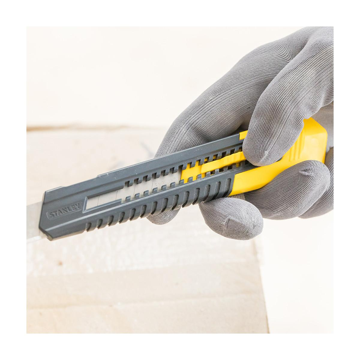 Eine graue behandschuhte Hand hält ein Stanley-Cuttermesser mit gelbem Schieber vor hellem Hintergrund.