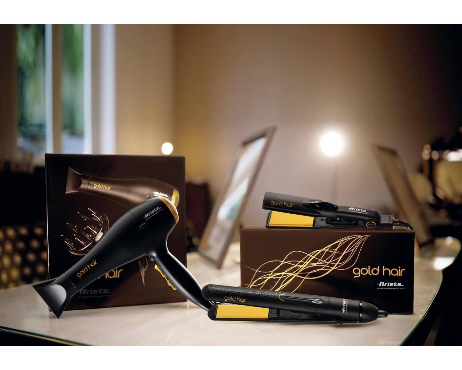 Black hairdryer and two hair straighteners with gold accents on a table.