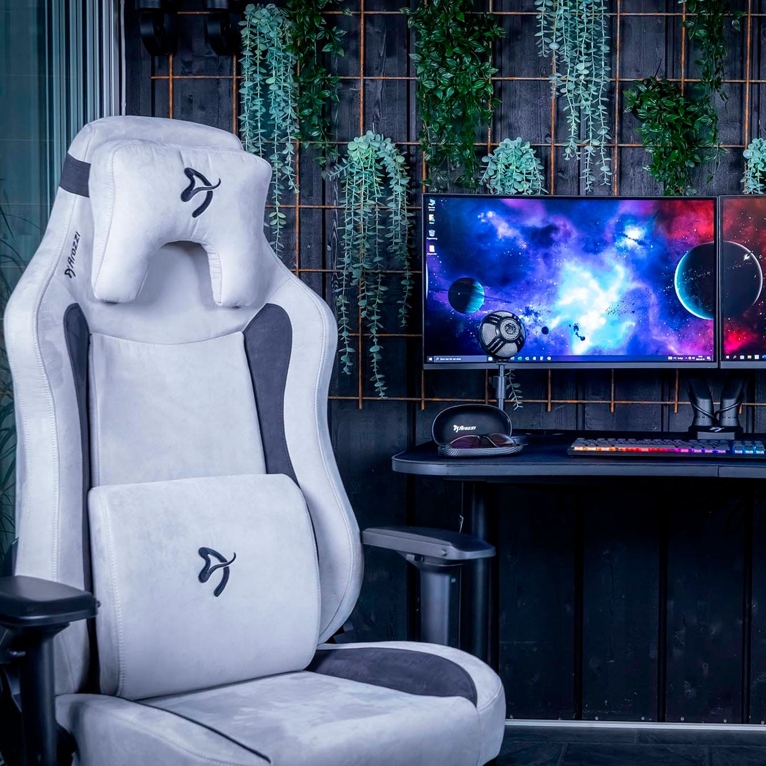 Ein weißer Gaming-Stuhl steht neben einem Schreibtisch mit zwei Monitoren, die Weltraumszenen zeigen.