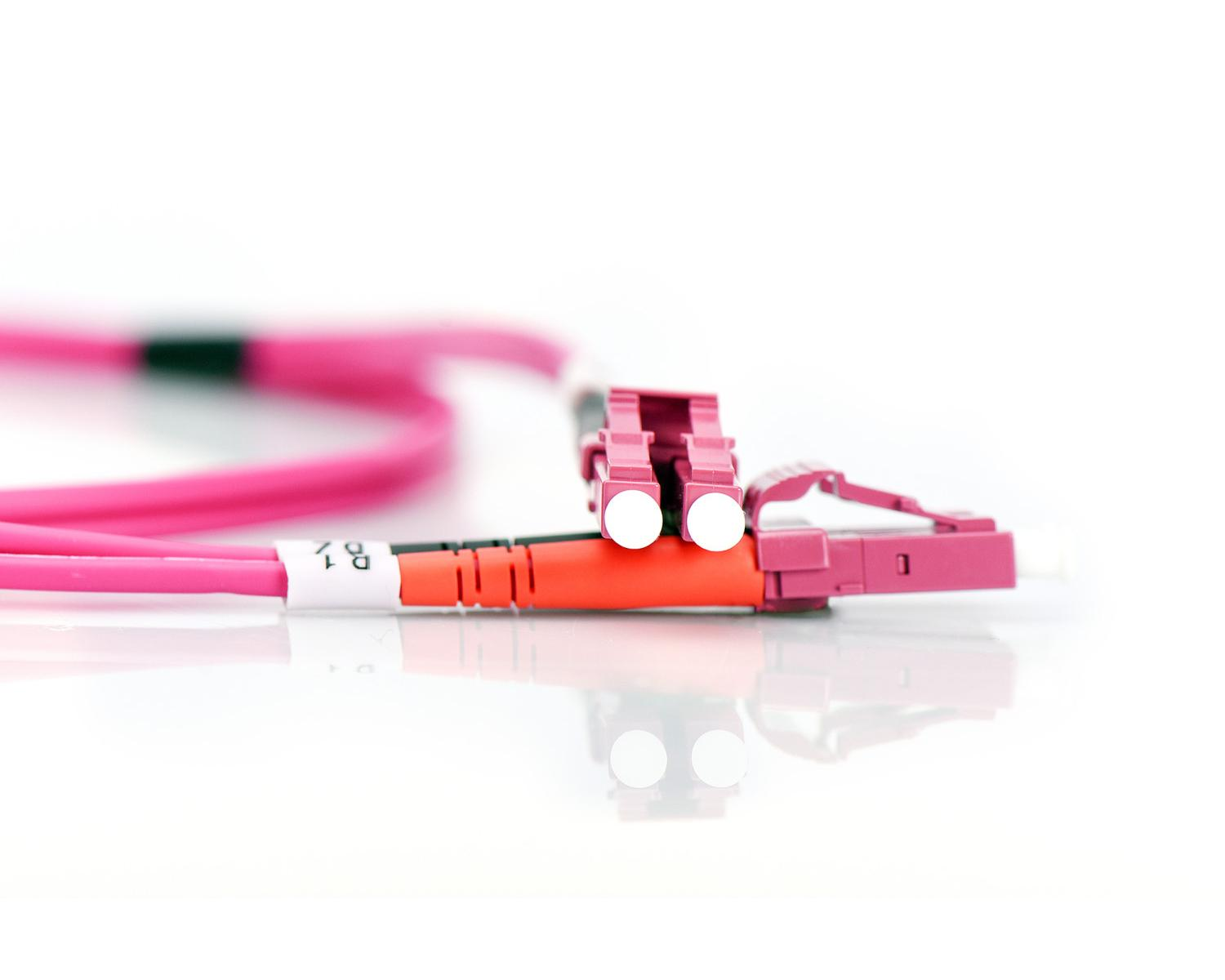Due cavi in fibra ottica rosa con connettori rosa e arancioni su superficie bianca.