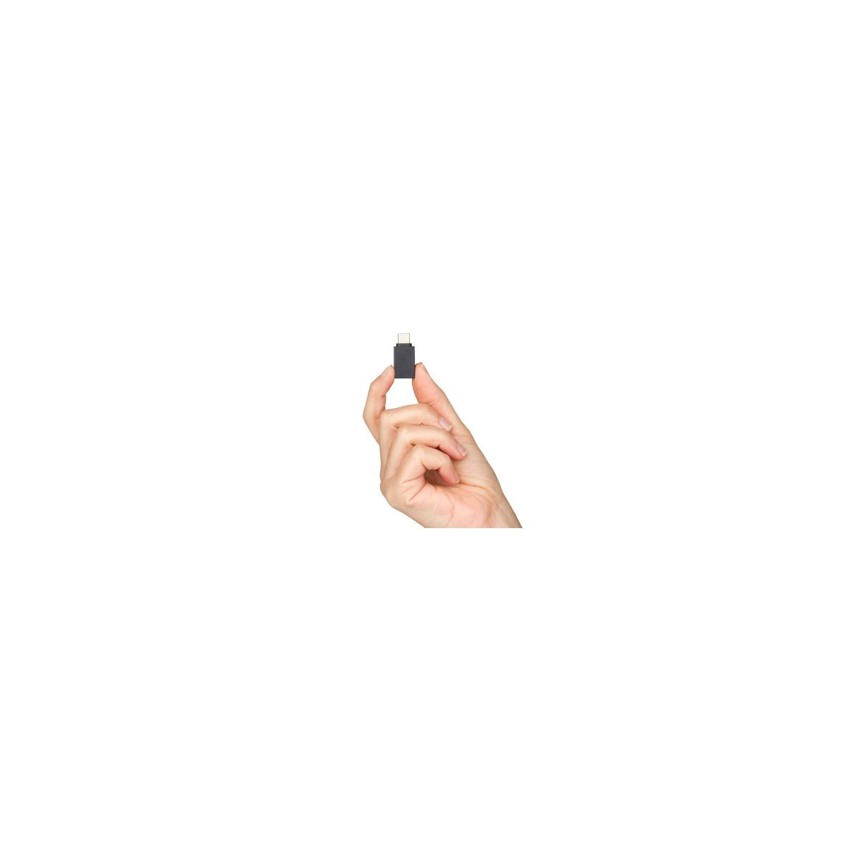 Dłoń trzyma mały, czarny adapter USB-C między kciukiem a palcem wskazującym.