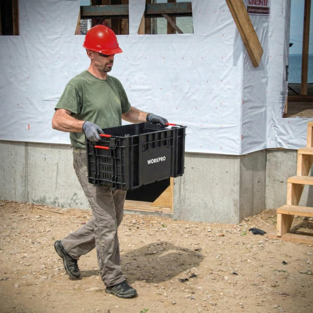 Kırmızı baretli adam inşaat alanında siyah WORKPRO kutu taşıyor.