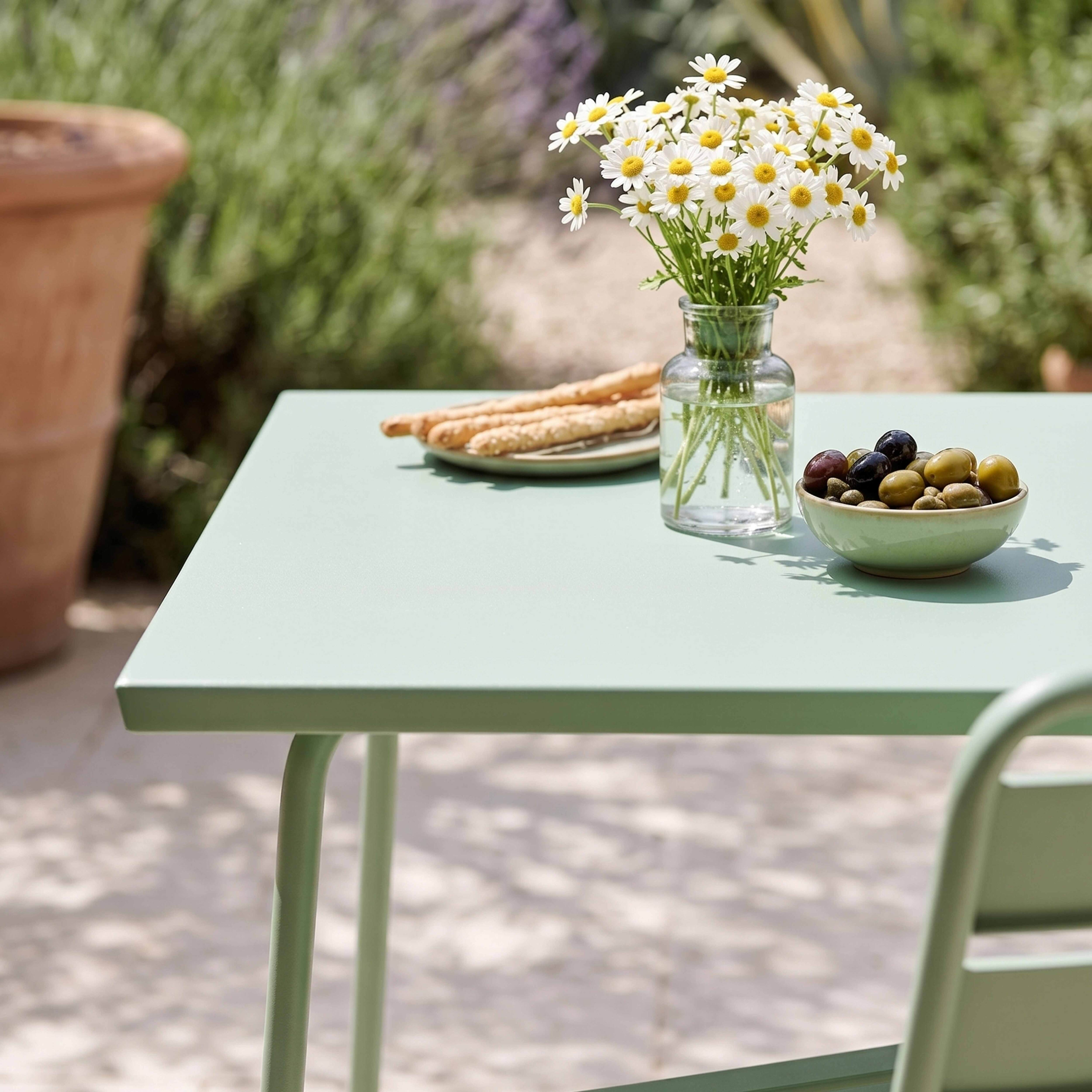 Ein grüner Tisch mit Blumen, Brot und Oliven im Freien.