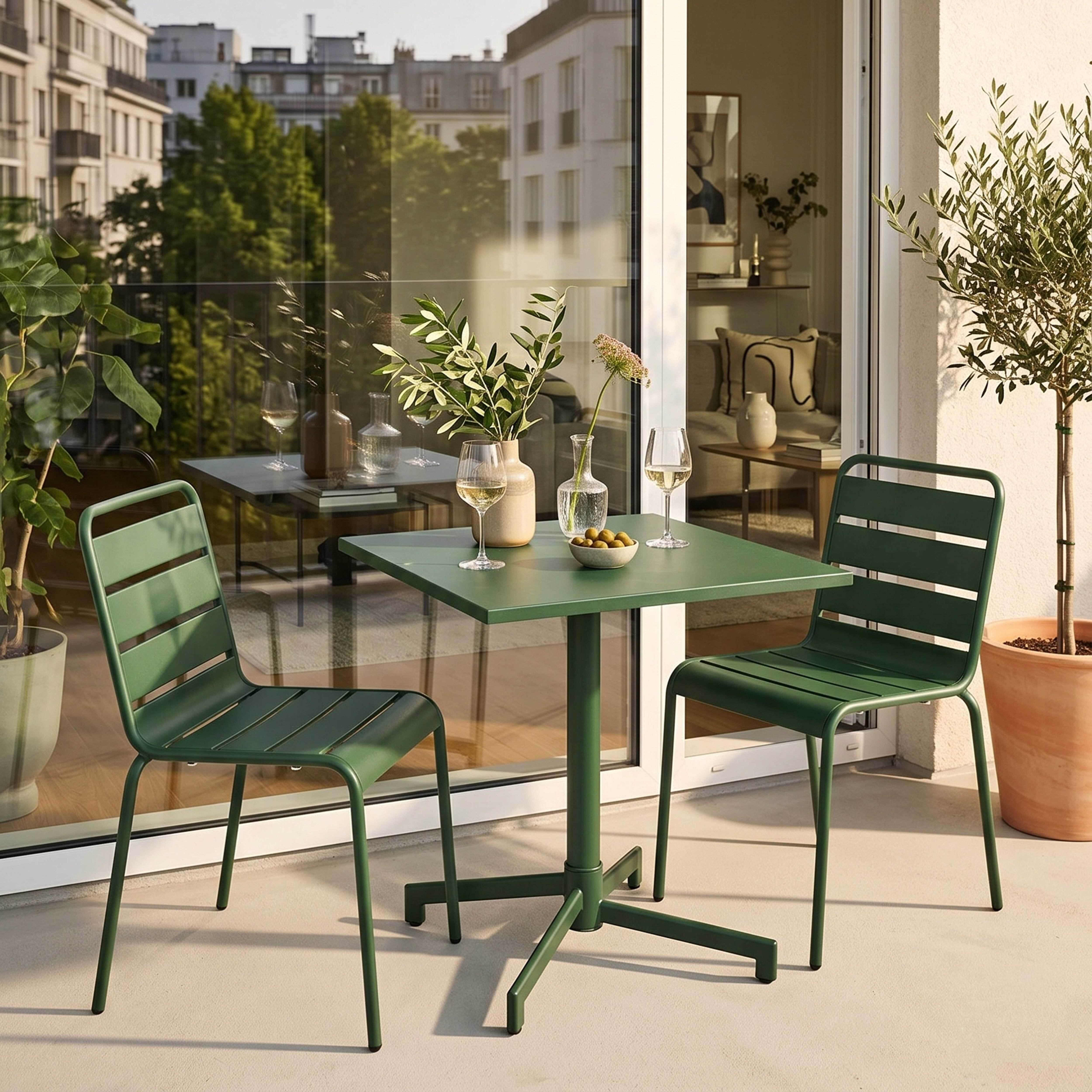 Ein grüner Tisch mit zwei Stühlen auf einem Balkon mit Stadtblick.