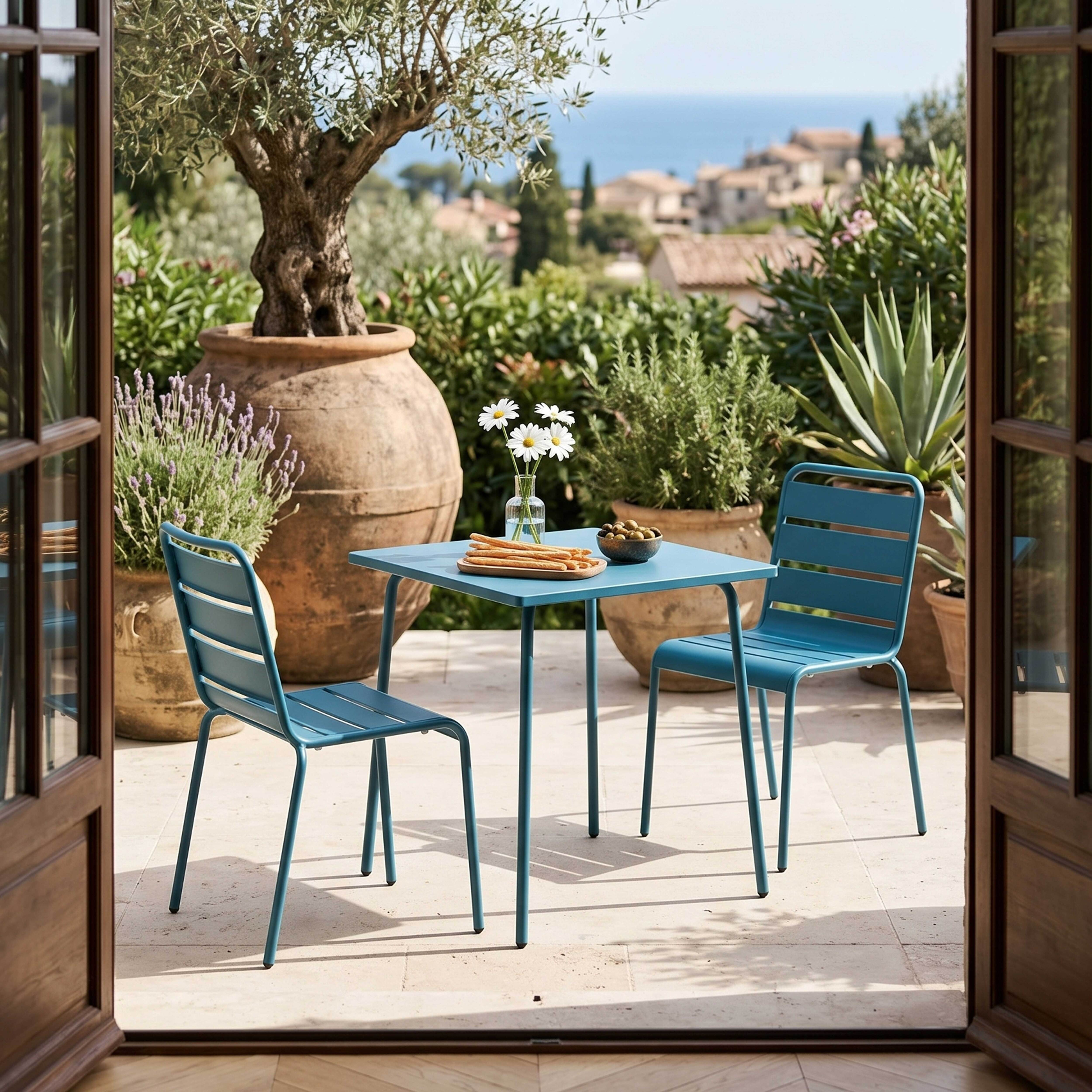 Blaue Gartenmöbel stehen auf einer Terrasse mit Blick auf das Meer und Häuser.