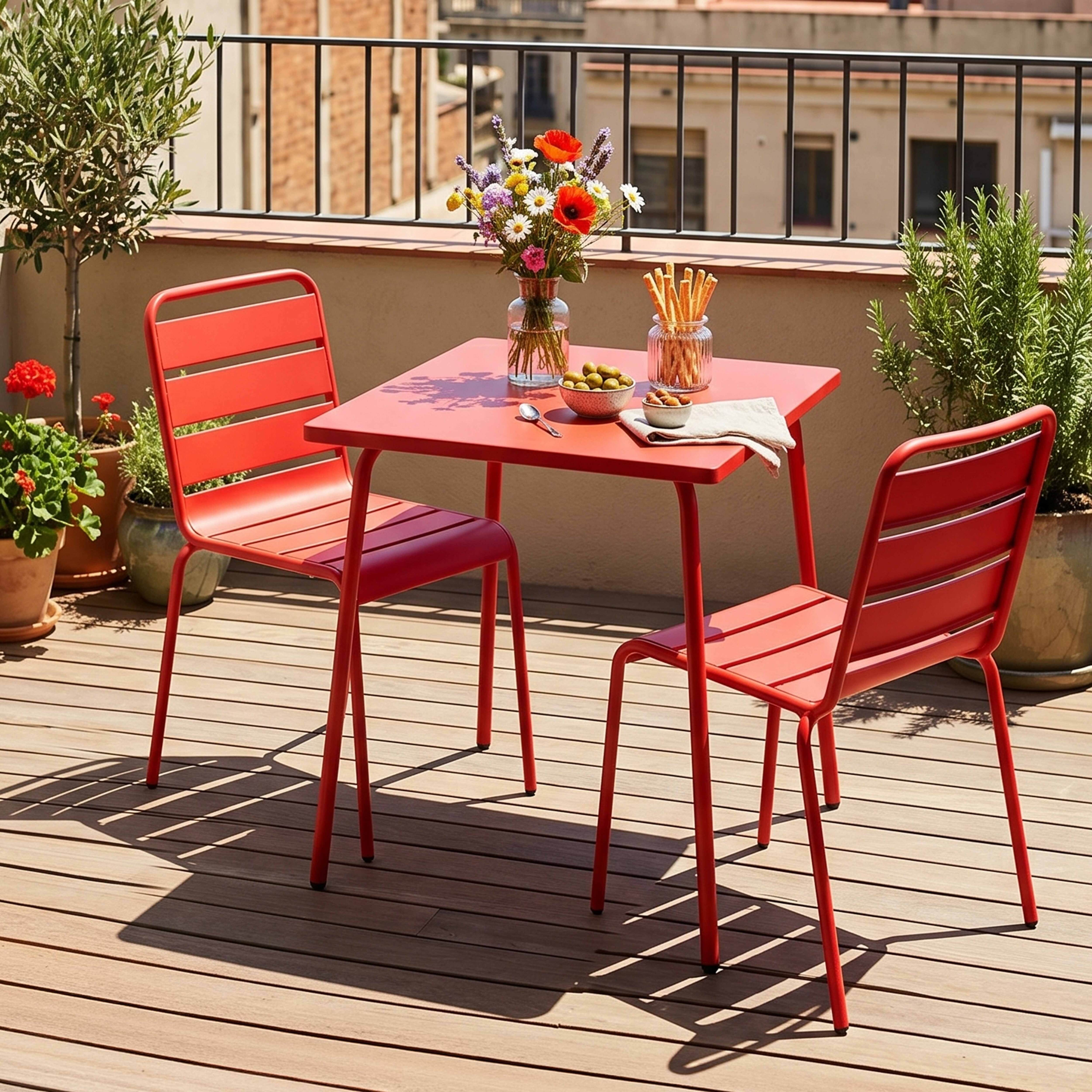 Roter Tisch und zwei Stühle auf Holzdeck mit Blumen und Snacks.