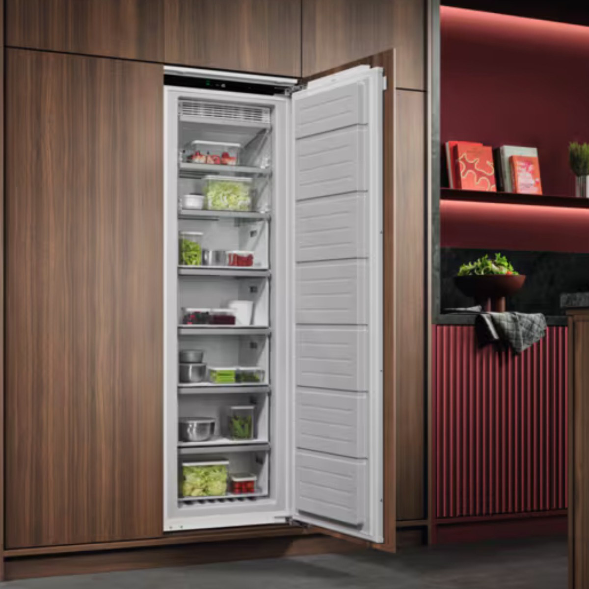 Un frigorífico abierto lleno de comida, dentro de un mueble de madera en una cocina moderna.