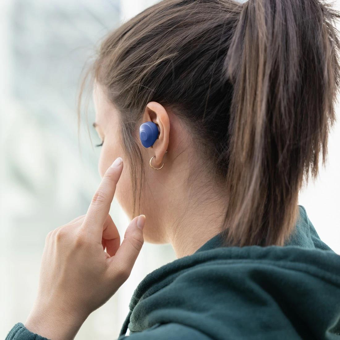 Eine Frau mit einem blauen Ohrhörer im Ohr, ihre Finger berühren ihr Ohr.