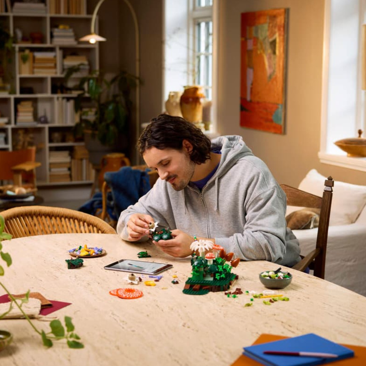 Un uomo costruisce un set Lego con funghi e piante su un tavolo.