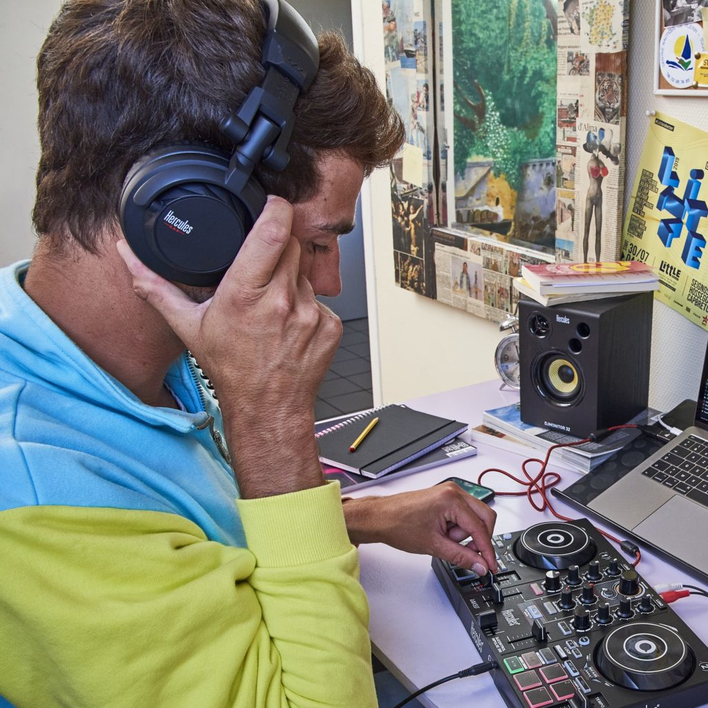 Ein Mann mit Kopfhörern bedient ein DJ-Pult, ein Laptop und ein Lautsprecher sind auf dem Schreibtisch.