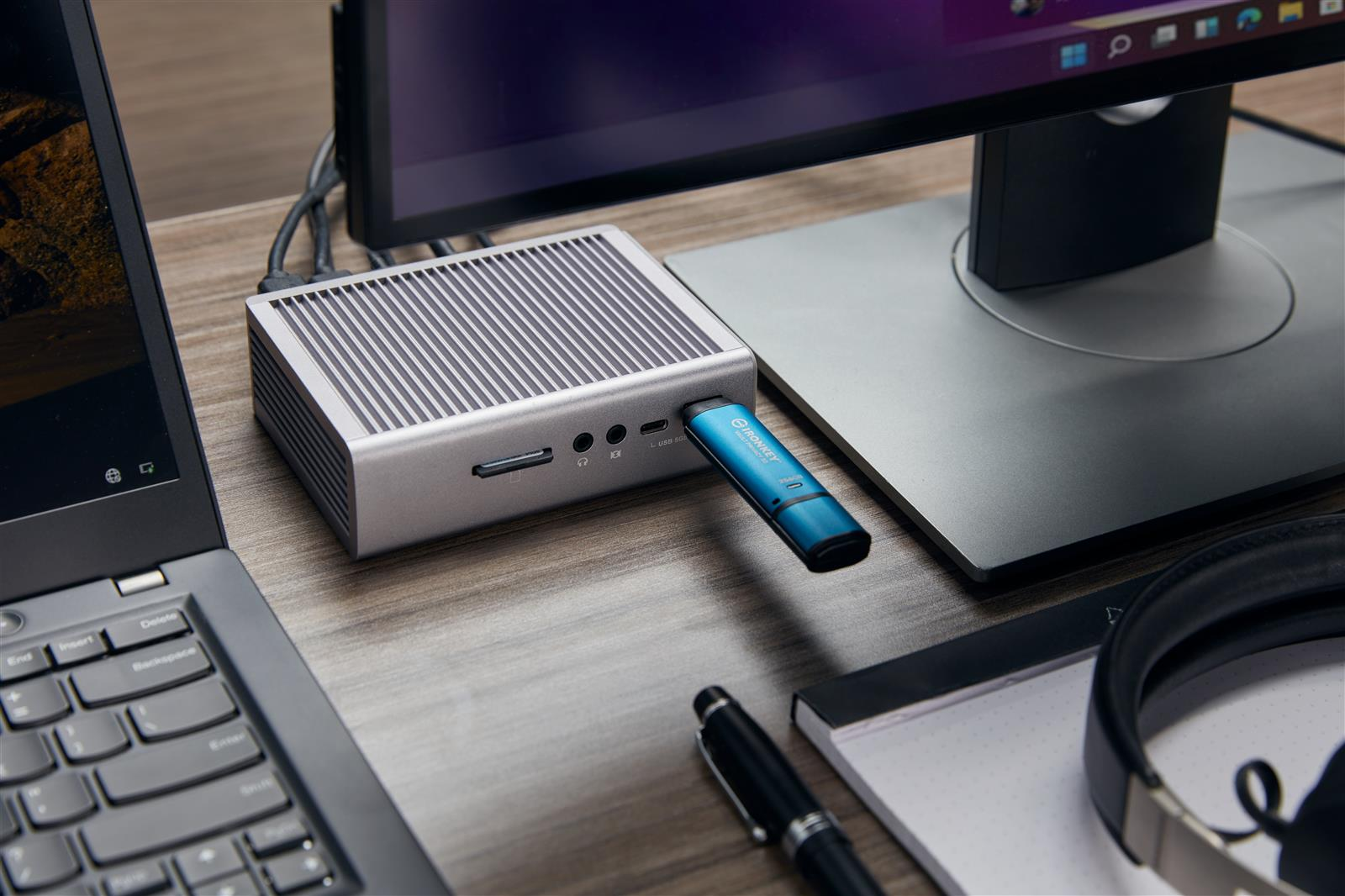 Un mini PC plateado con una unidad USB azul insertada junto a un portátil.