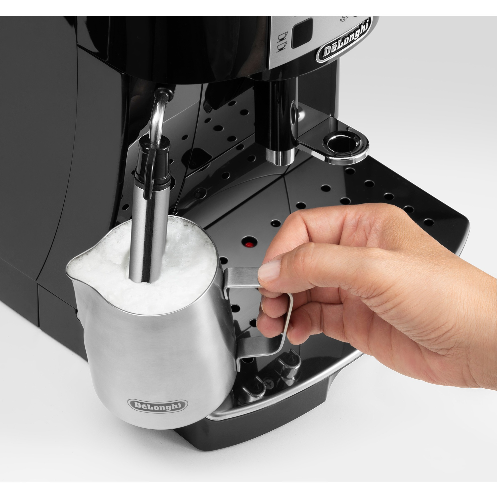 Eine Hand hält einen Metallkrug mit geschäumter Milch unter einer Kaffeemaschine.
