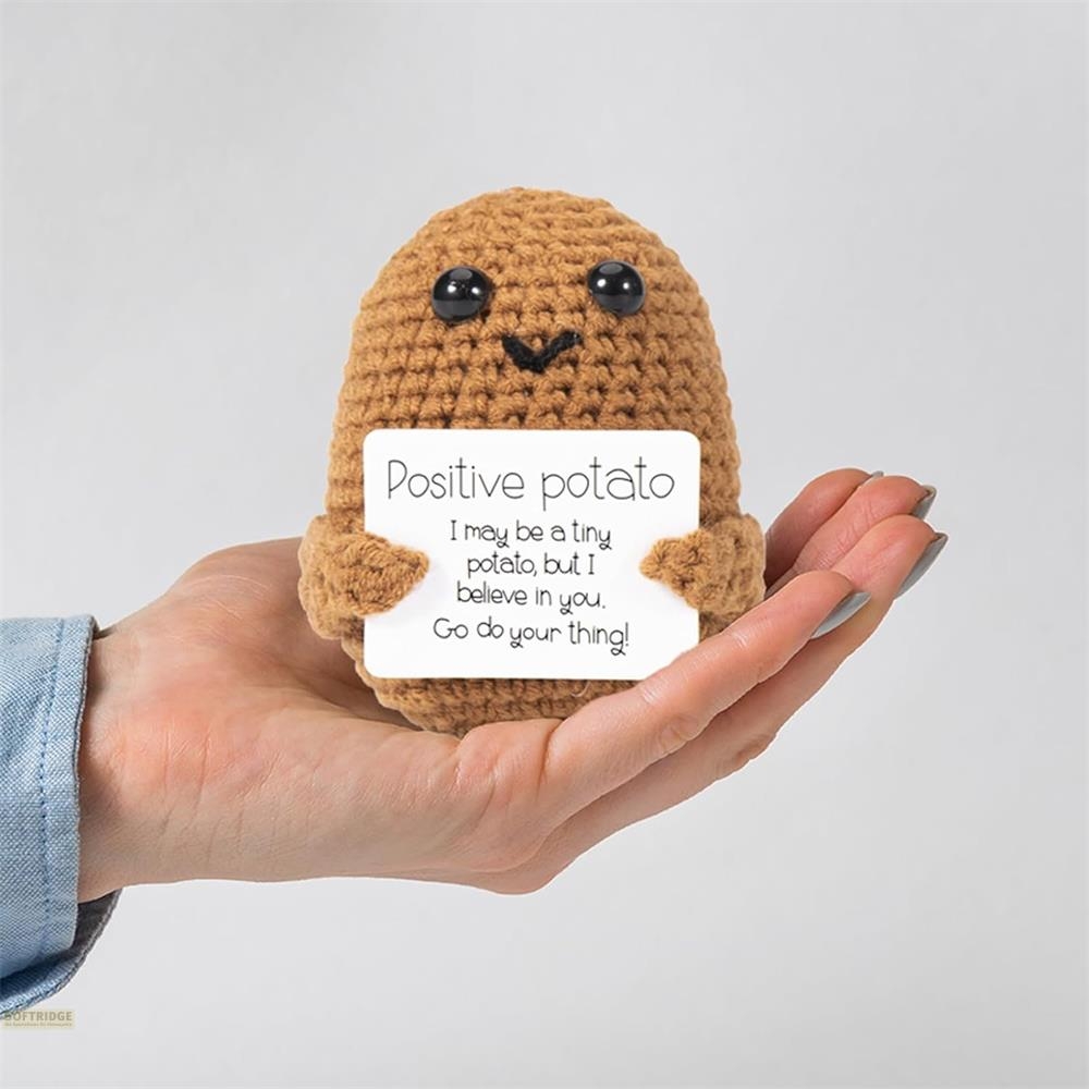 Gehäkelte braune Kartoffel hält ein Schild mit der Aufschrift „Positive Kartoffel“. Auf einer Hand.