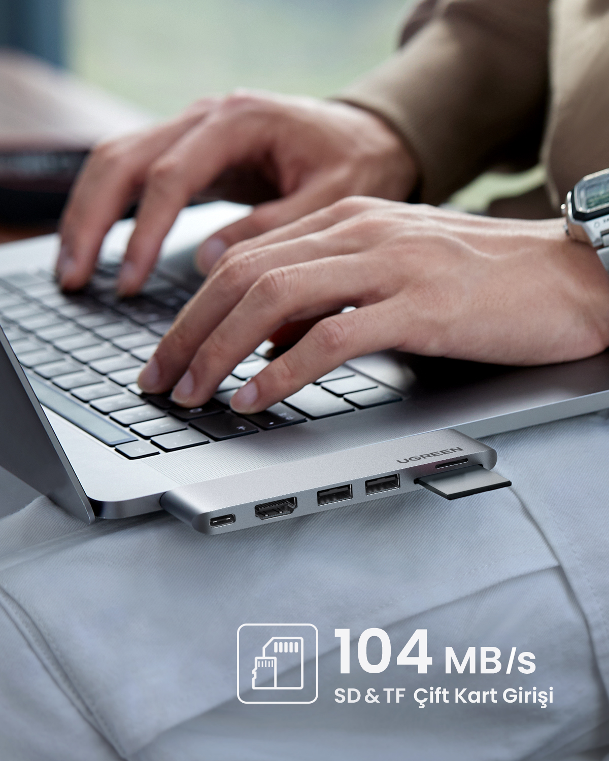 Kişi dizüstü bilgisayarda yazıyor, SD kartlı USB-C hub takılı.