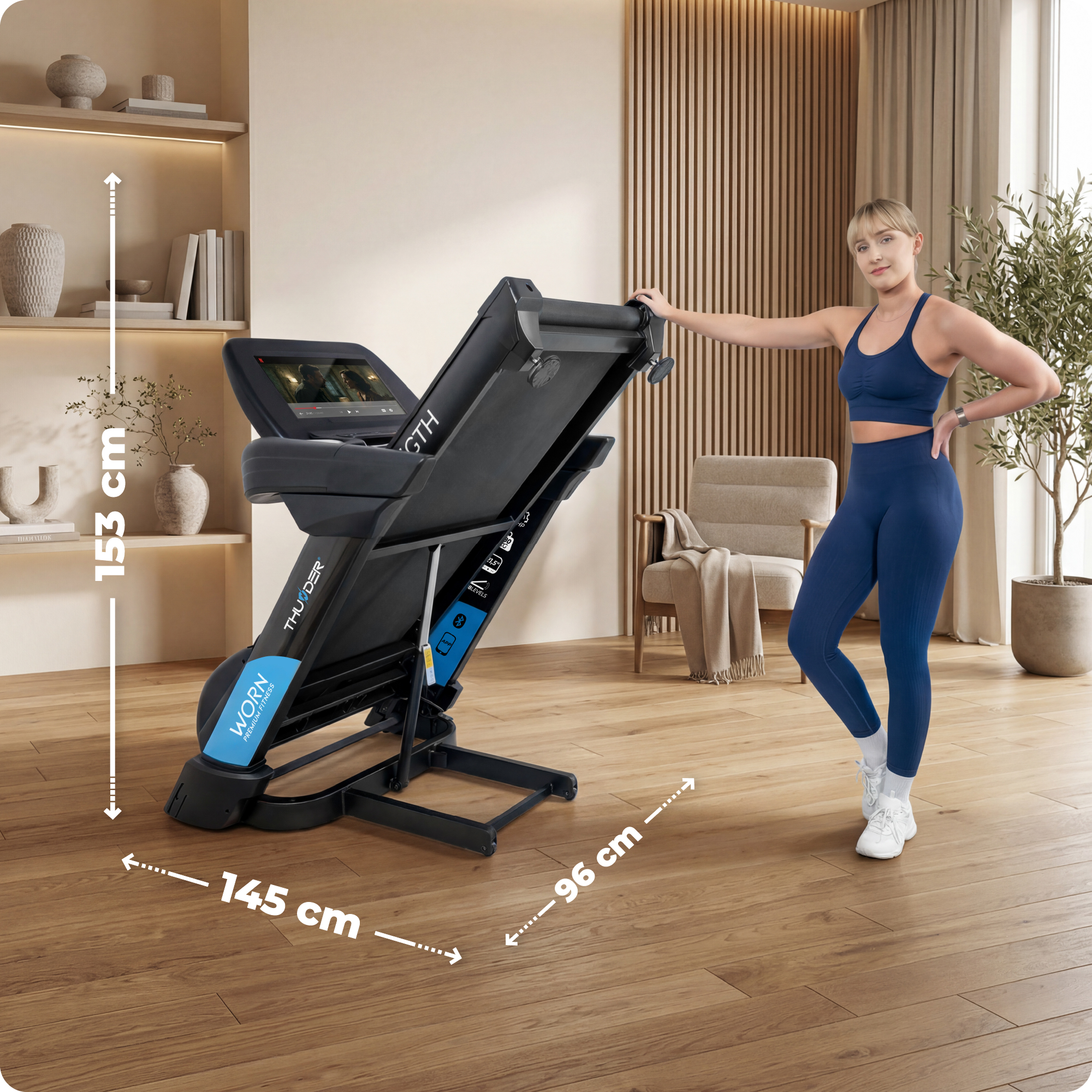 Eine Frau in blauer Sportkleidung steht neben einem zusammengeklappten Laufband.