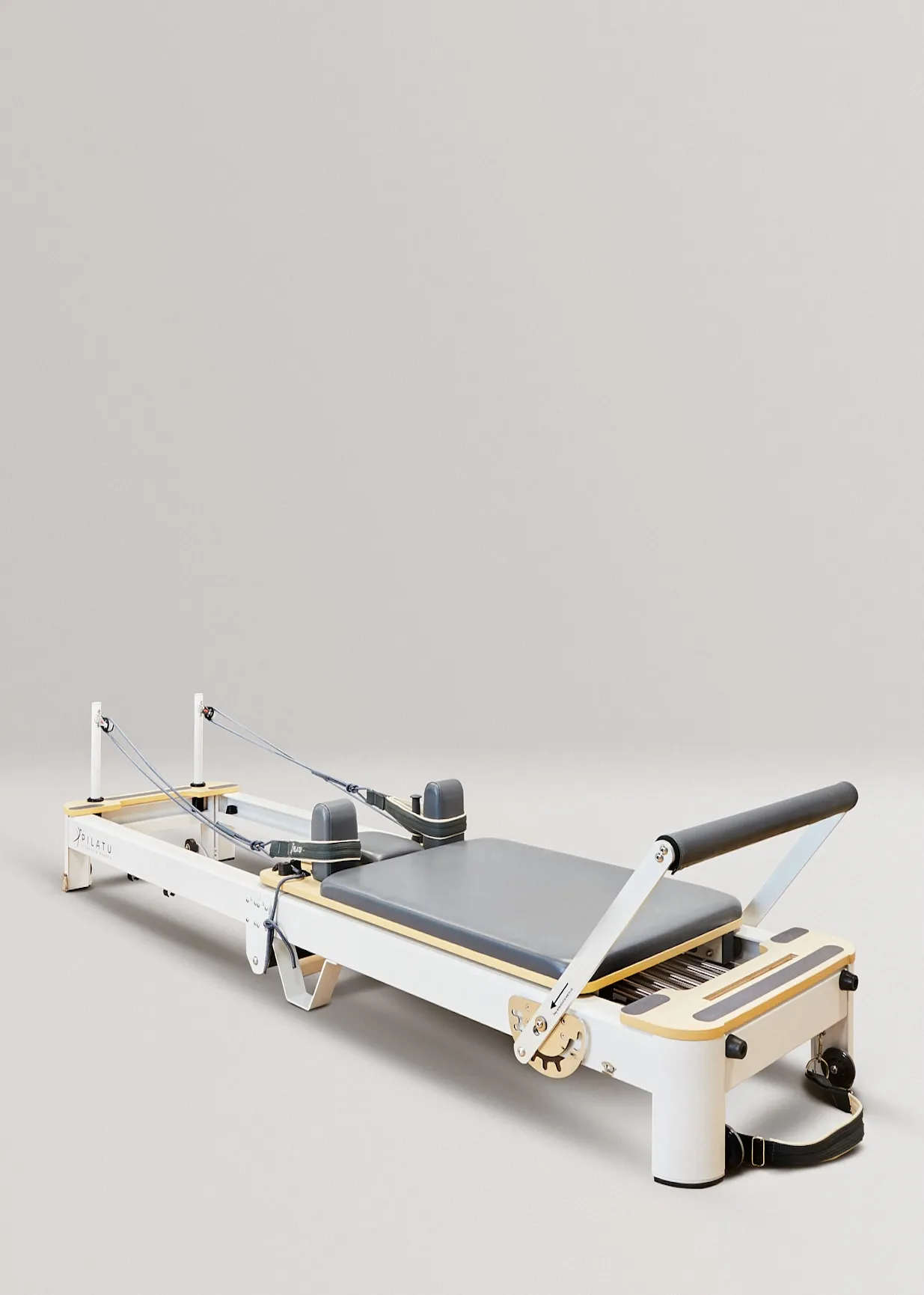 Una máquina reformadora de Pilates blanca y de madera con acolchado gris y asas negras.