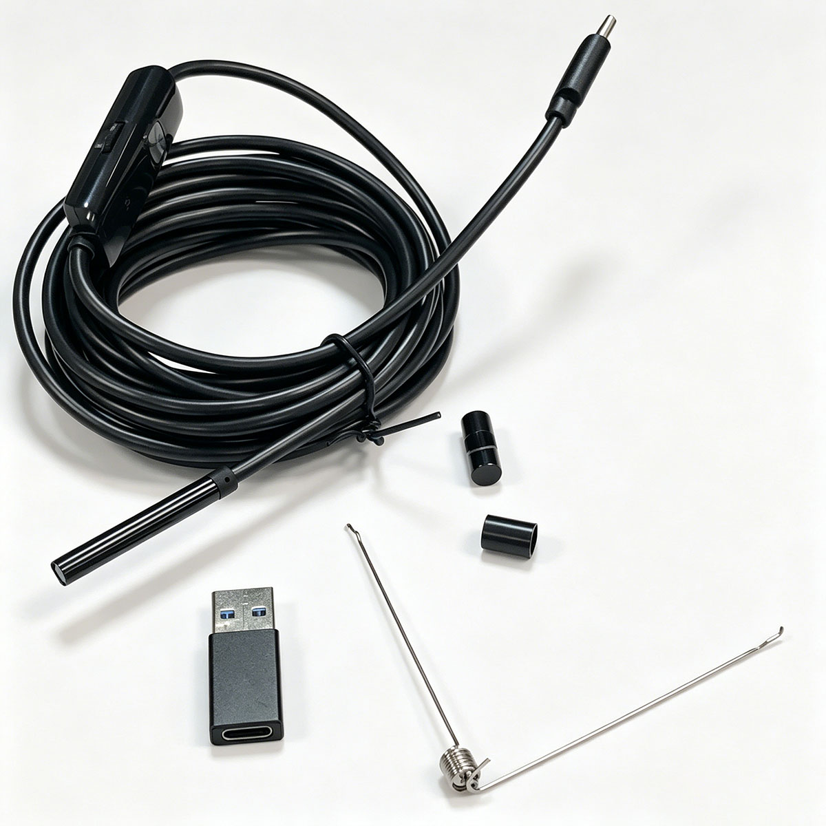 Ein aufgerolltes schwarzes Kabel mit Kamerakopf, USB-Adapter und kleinen Aufsätzen auf weißem Untergrund.