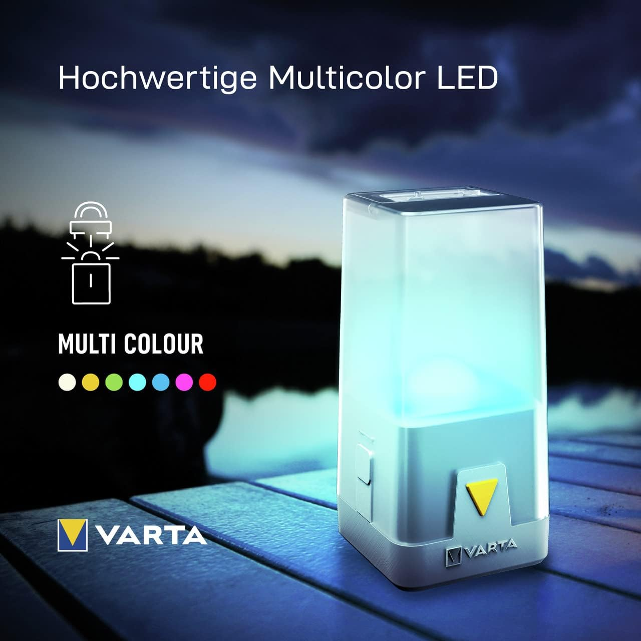 Una lanterna LED multicolore Varta brilla blu-verde su un tavolo di legno all'aperto.