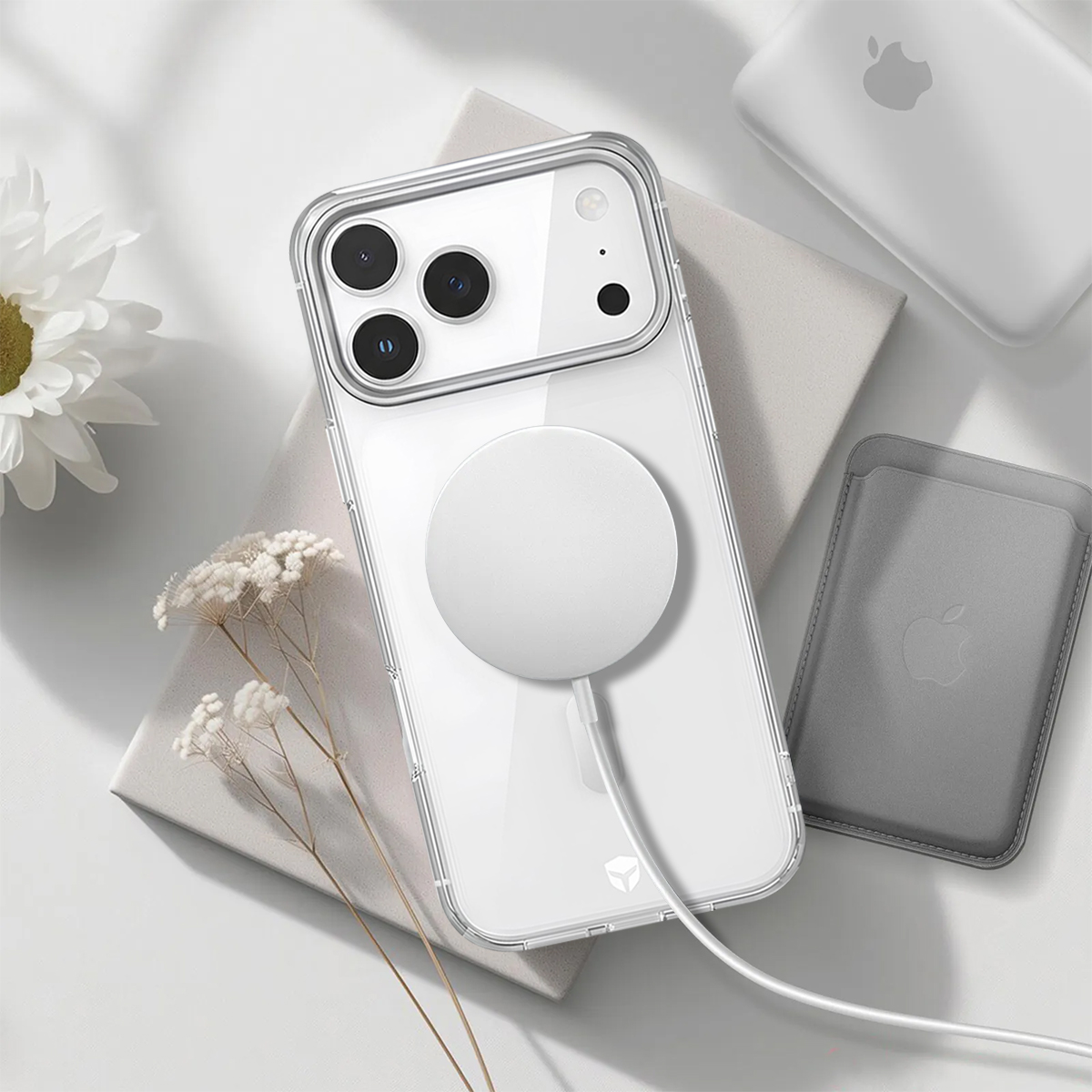 Klare iPhone-Hülle mit weißem MagSafe-Ladegerät und Trockenblumen auf hellem Grund.