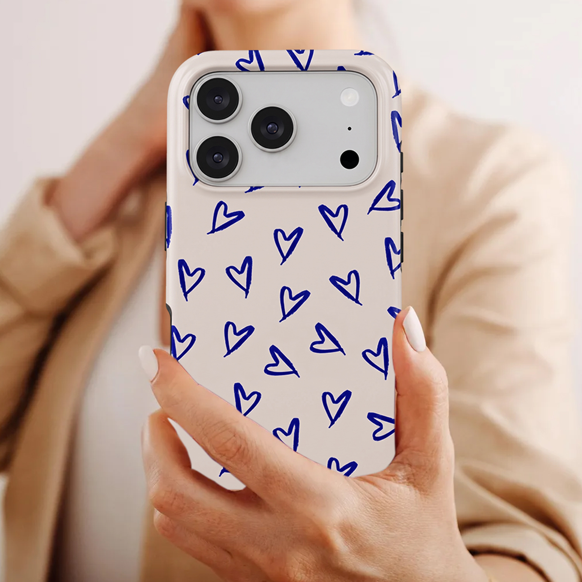 Una persona sostiene un teléfono con funda beige claro con corazones azules.