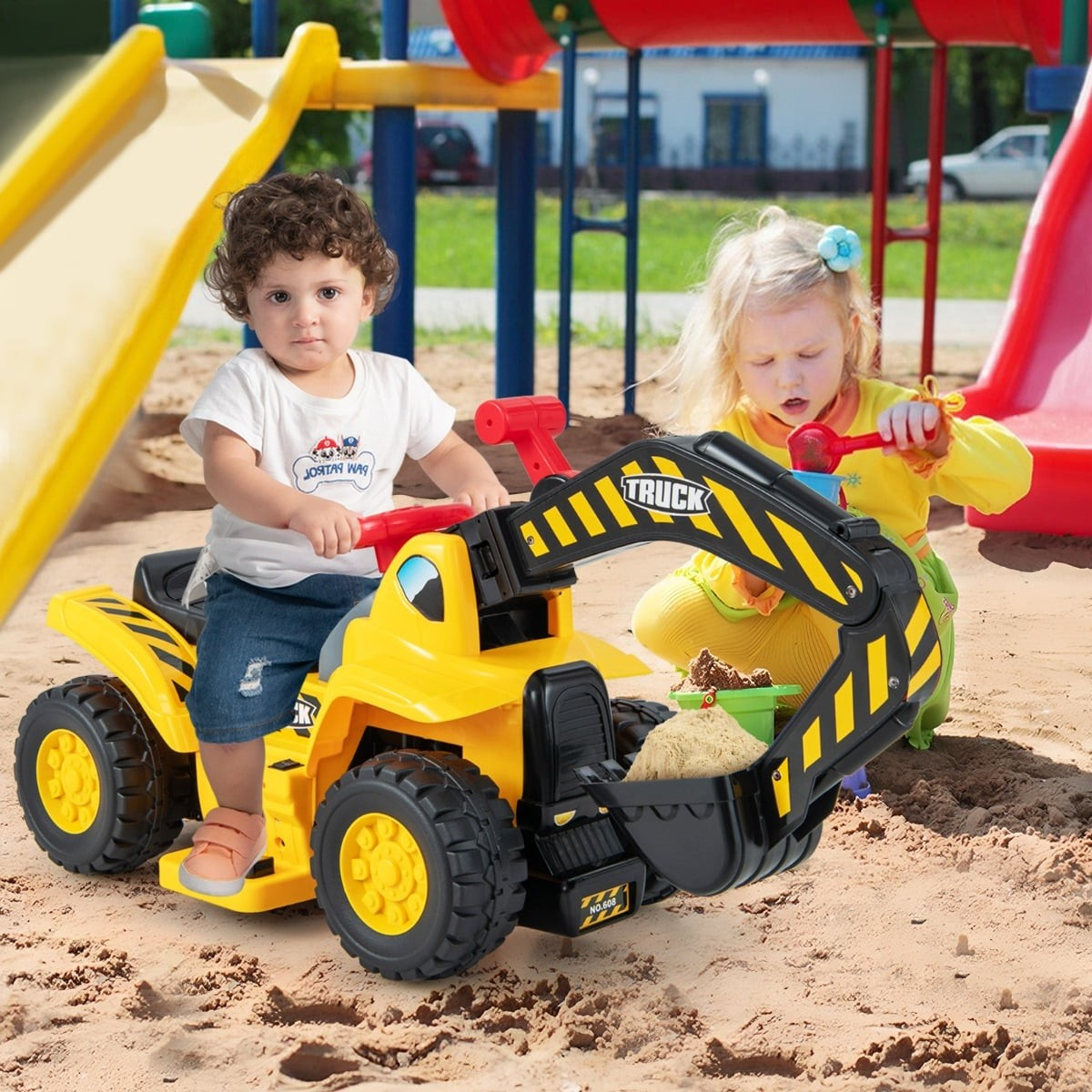 Two children play on a playground with a yellow toy digger truck.