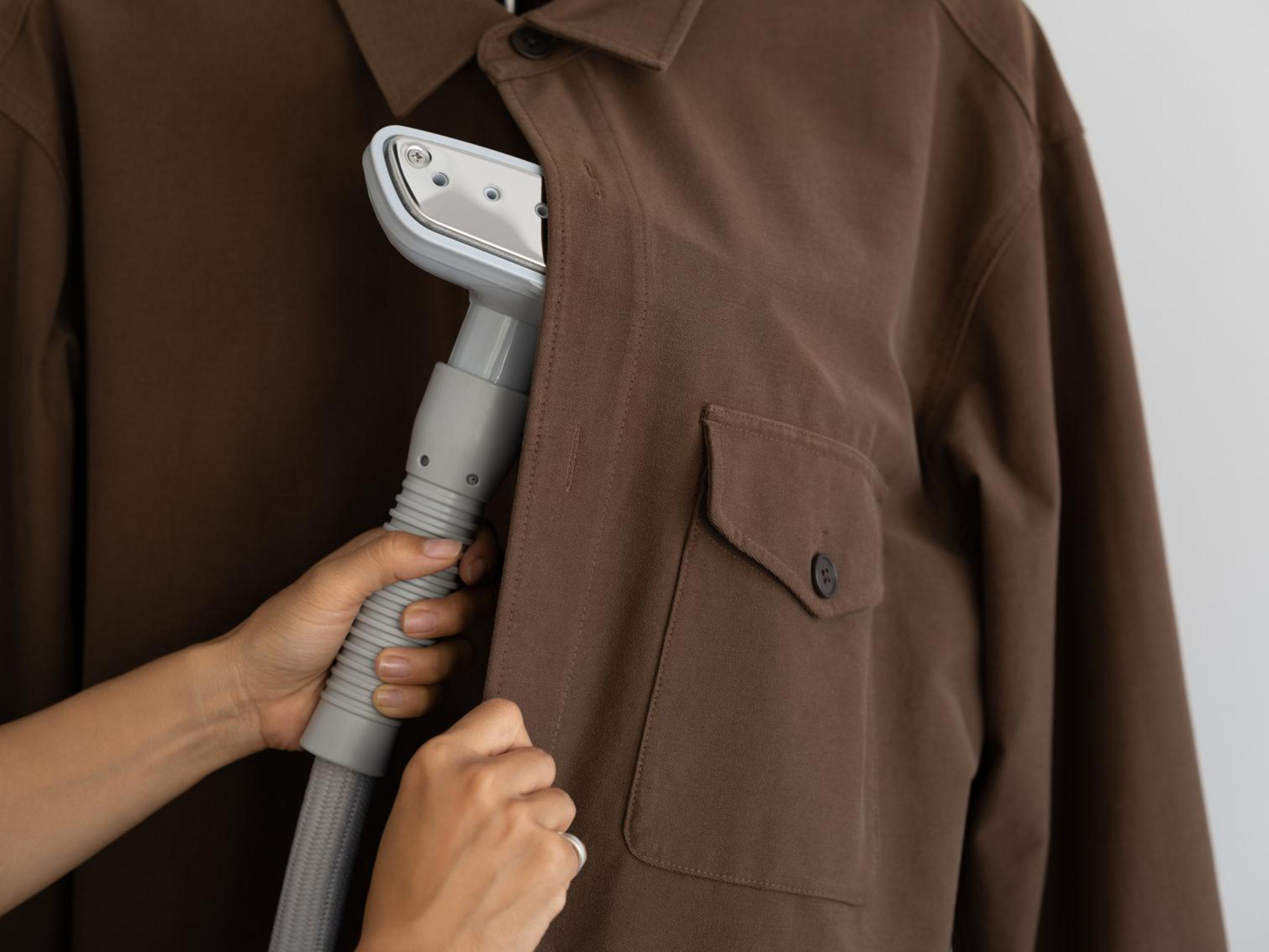 Persona stira giacca marrone con vaporizzatore.
