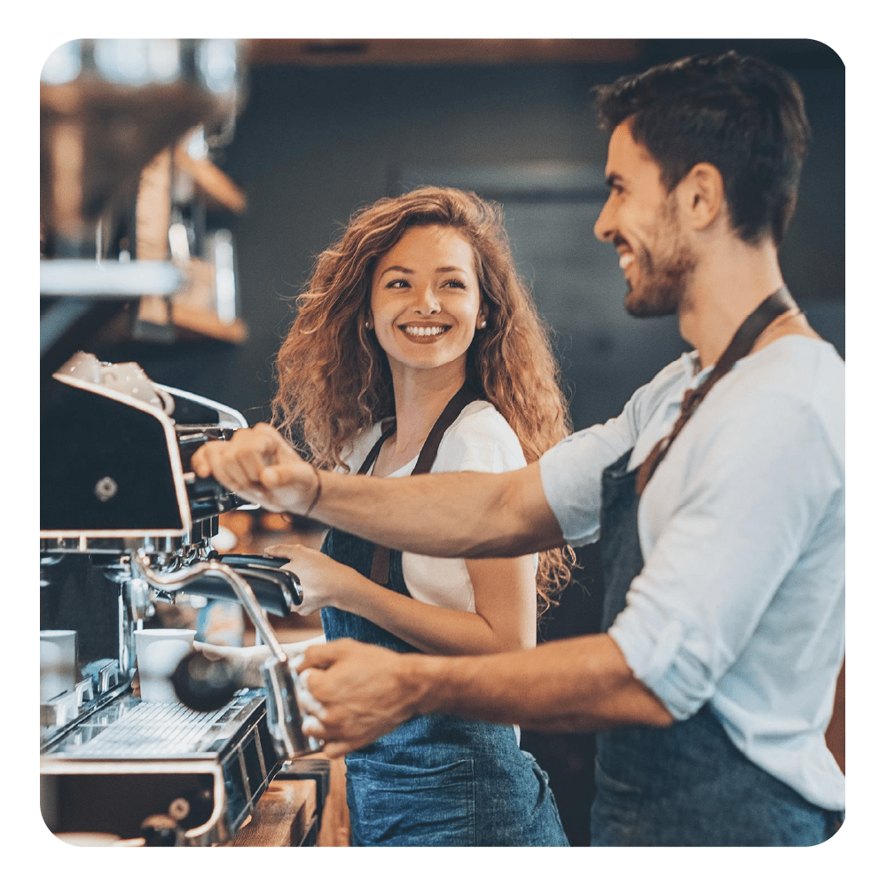 Homme et femme en tabliers se sourient en préparant du café.