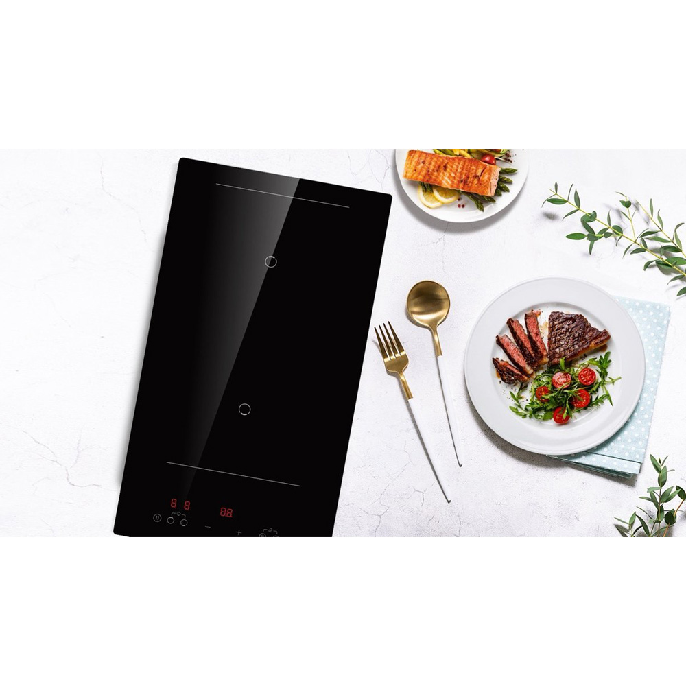 A black induction cooktop next to plates of food and cutlery.