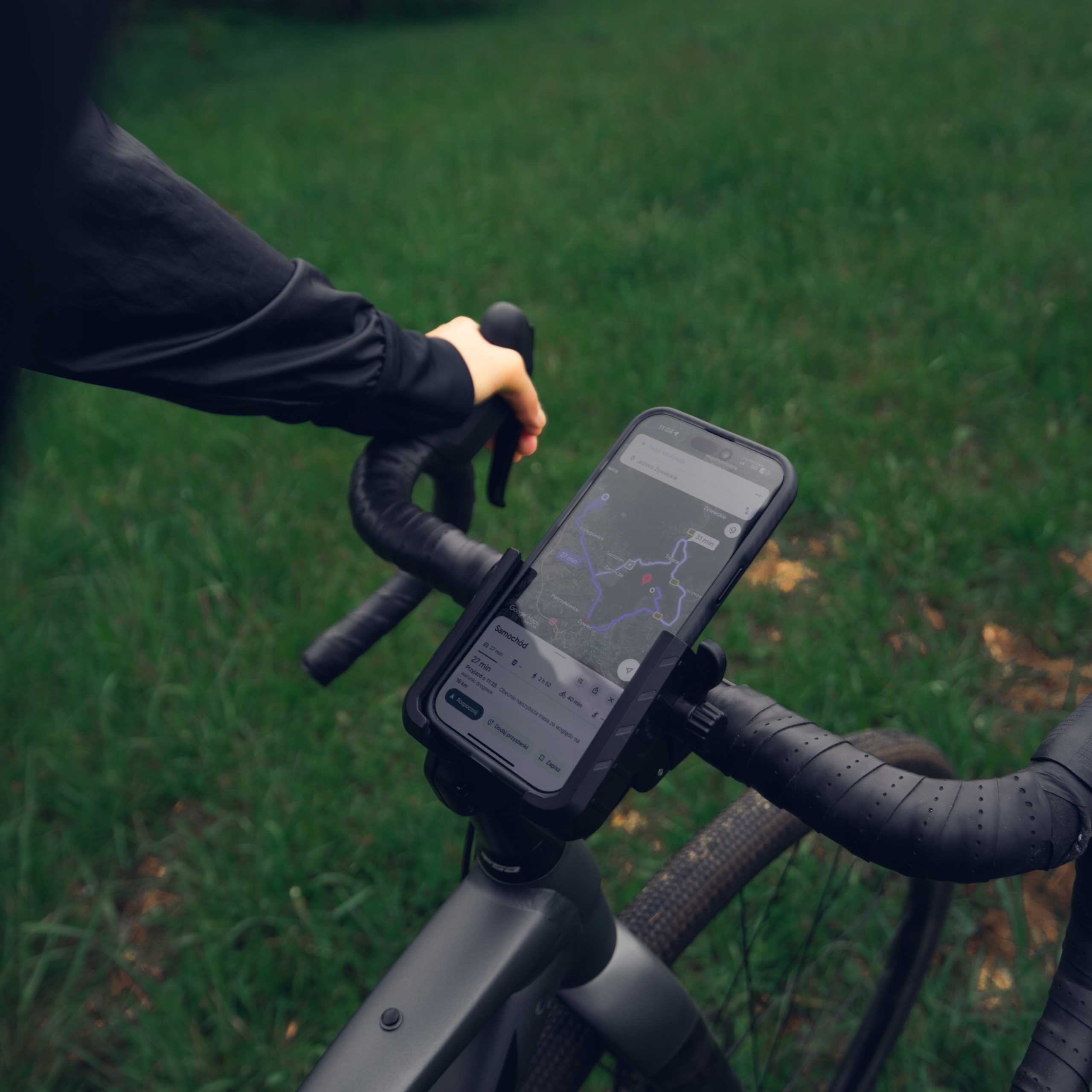 Kierownica rowerowa z uchwytem na telefon, pokazująca aplikację nawigacyjną na smartfonie na zewnątrz.