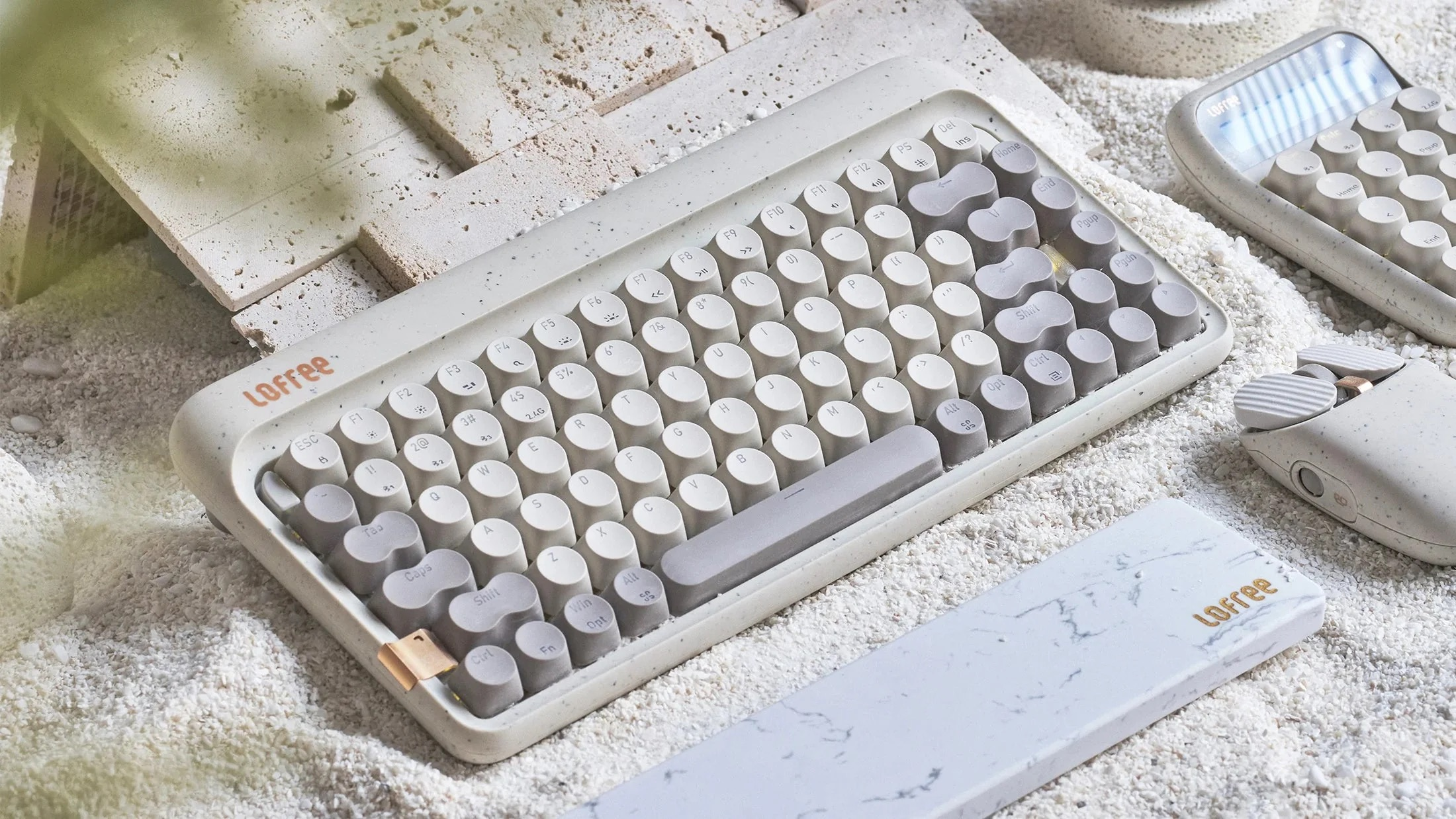 Klawiatura i mysz w stylu retro na białym piasku, z kamiennymi płytami w tle.
