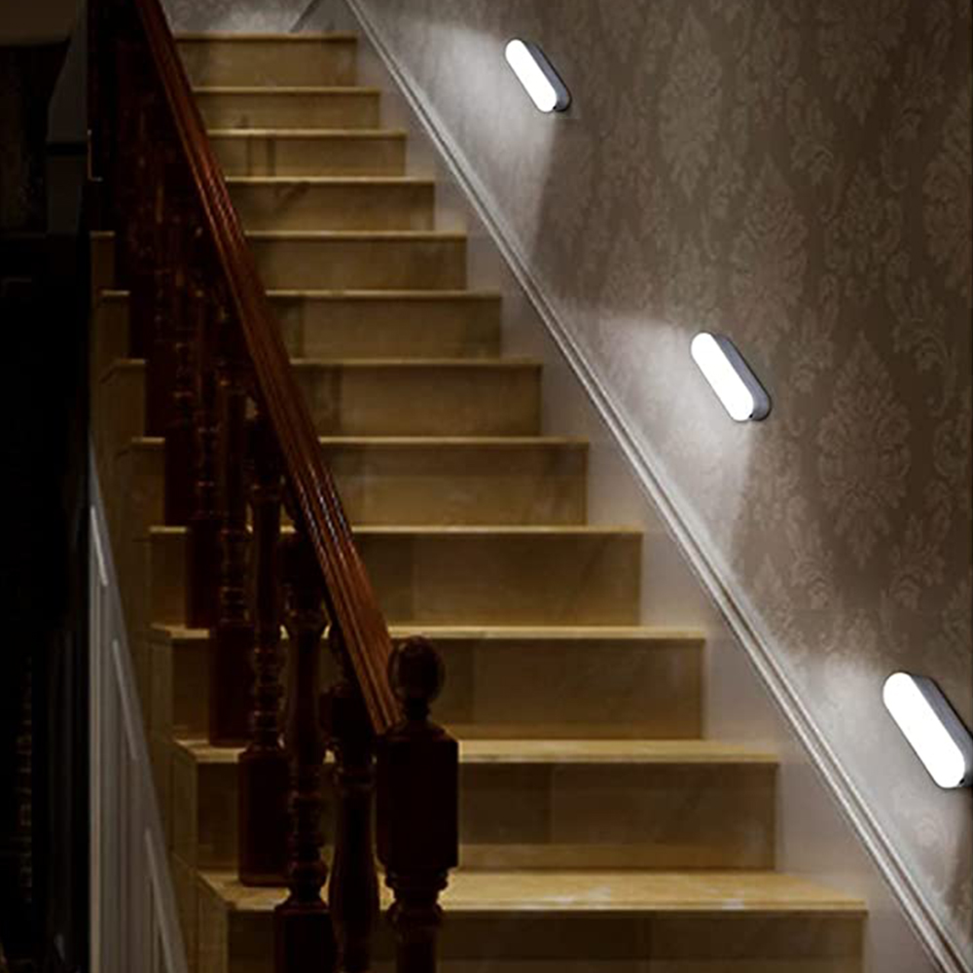 Holztreppe mit dunklem Geländer und Wandleuchten an der gemusterten Tapete.