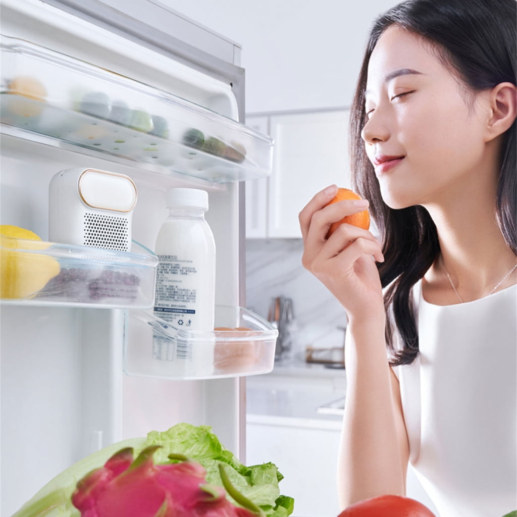 Eine Frau hält eine Orange vor einem Kühlschrank mit Lebensmitteln.