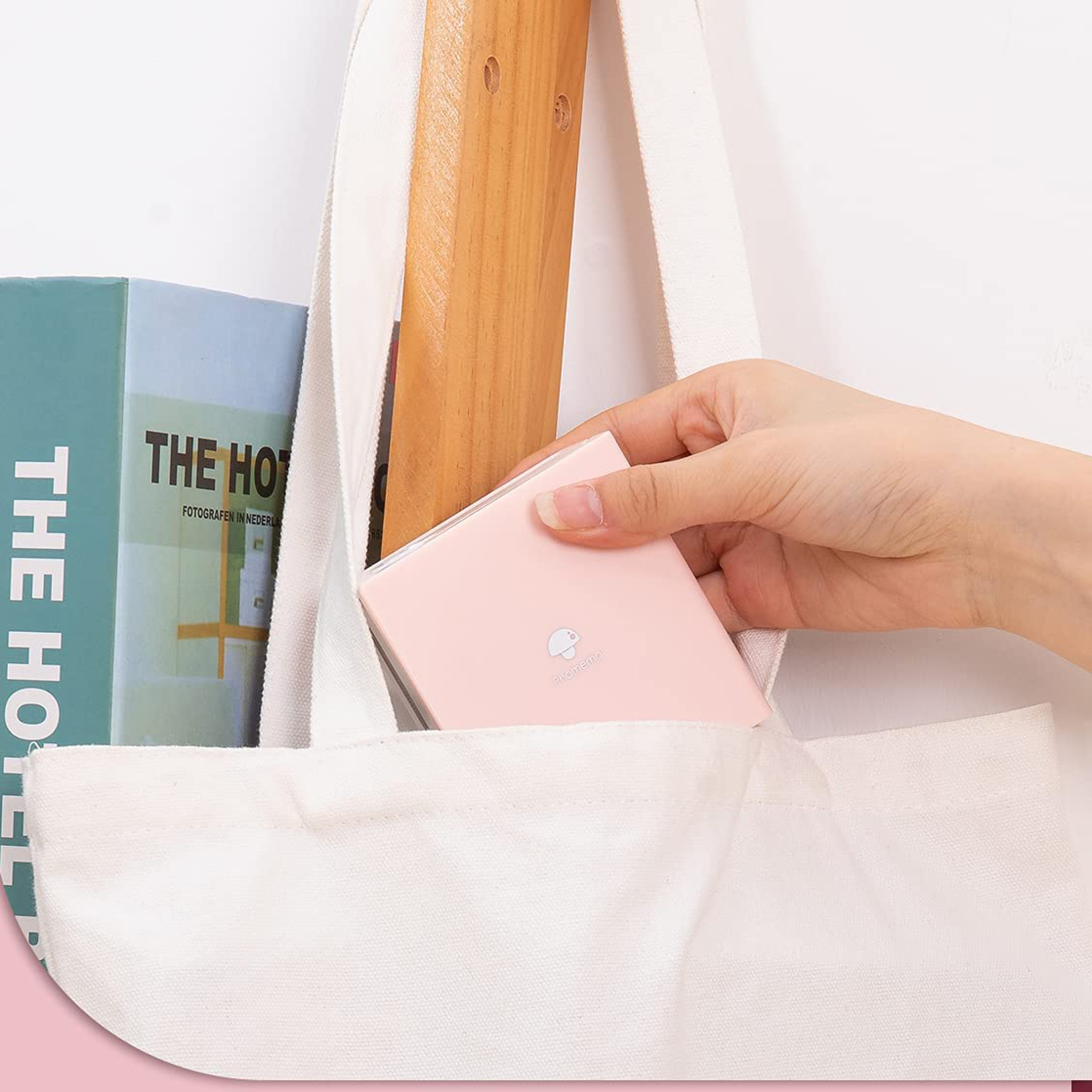 Eine Hand legt einen kleinen rosa Gegenstand in eine weiße Tasche neben zwei Büchern.