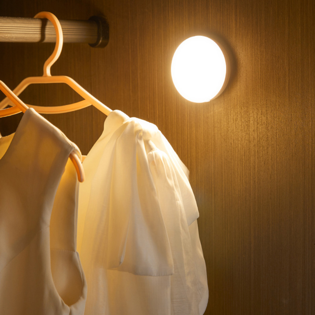 Ein helles Licht beleuchtet zwei weiße Kleidungsstücke auf Kleiderbügeln in einem Schrank.