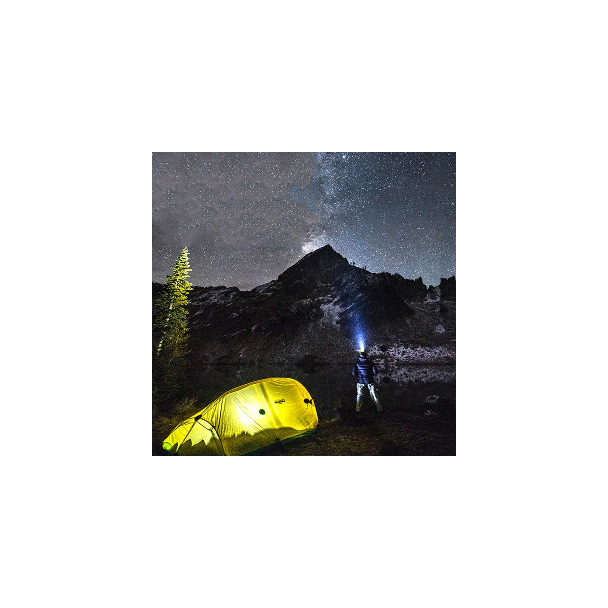 Ein gelbes Zelt leuchtet unter einem Sternenhimmel, ein Mann mit Stirnlampe steht daneben.