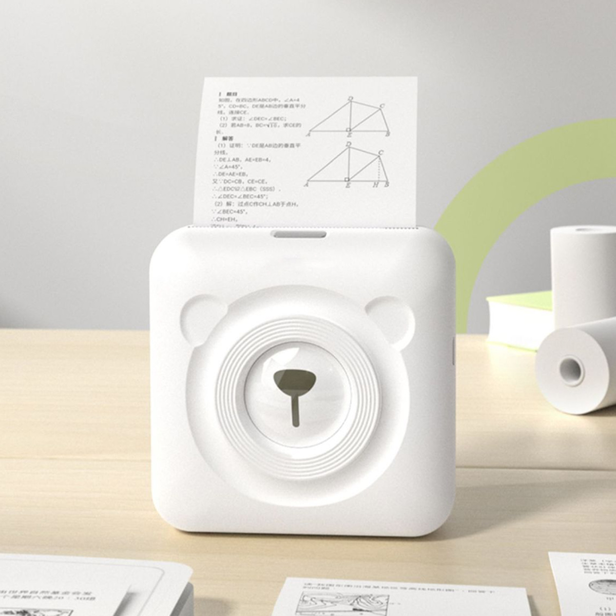 Ein weißer Mini-Drucker mit Teddybär-Gesicht druckt ein Blatt Papier mit geometrischen Diagrammen.