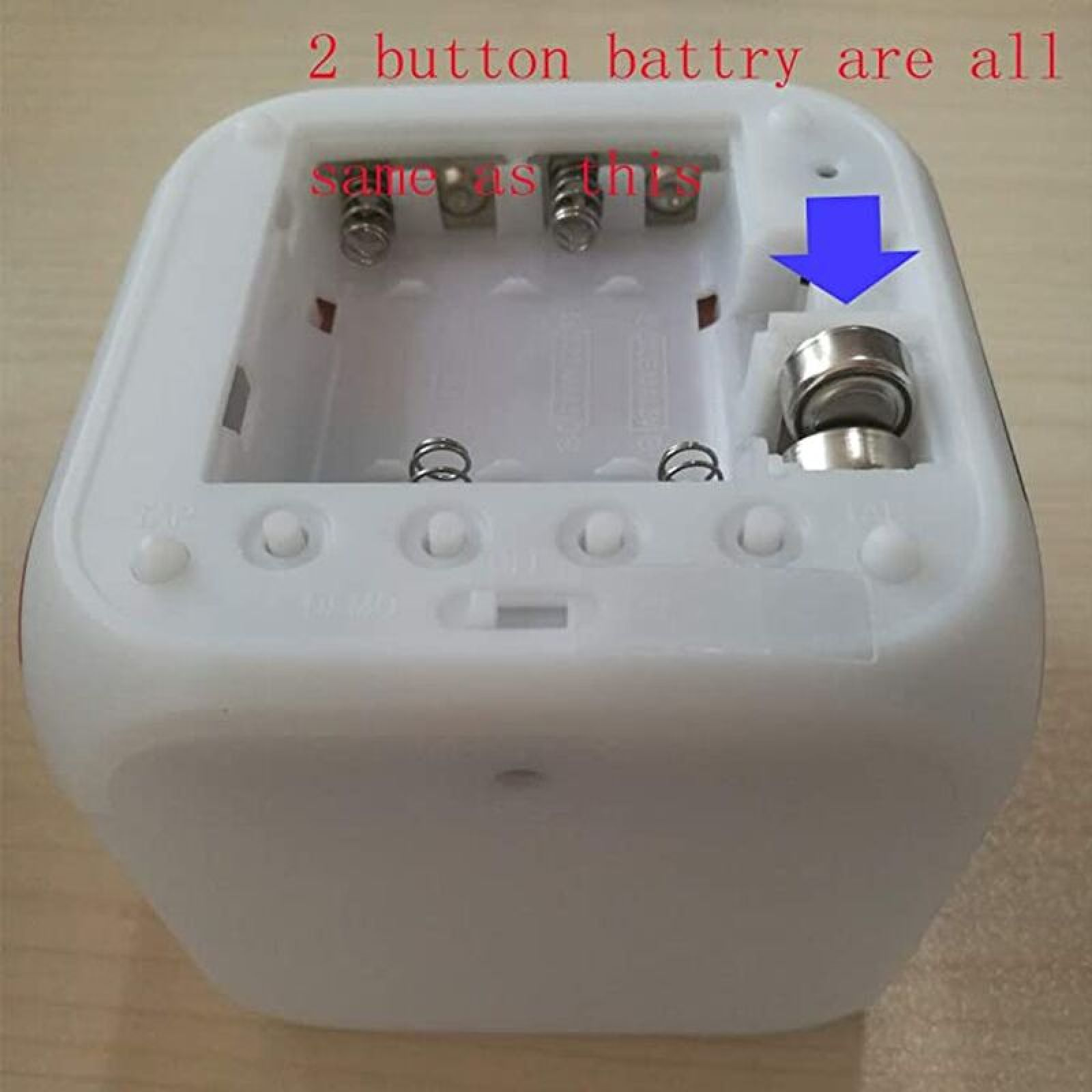 Ein weißer Wecker ohne Batterien, mit einem blauen Pfeil, der auf eine Knopfzelle zeigt.