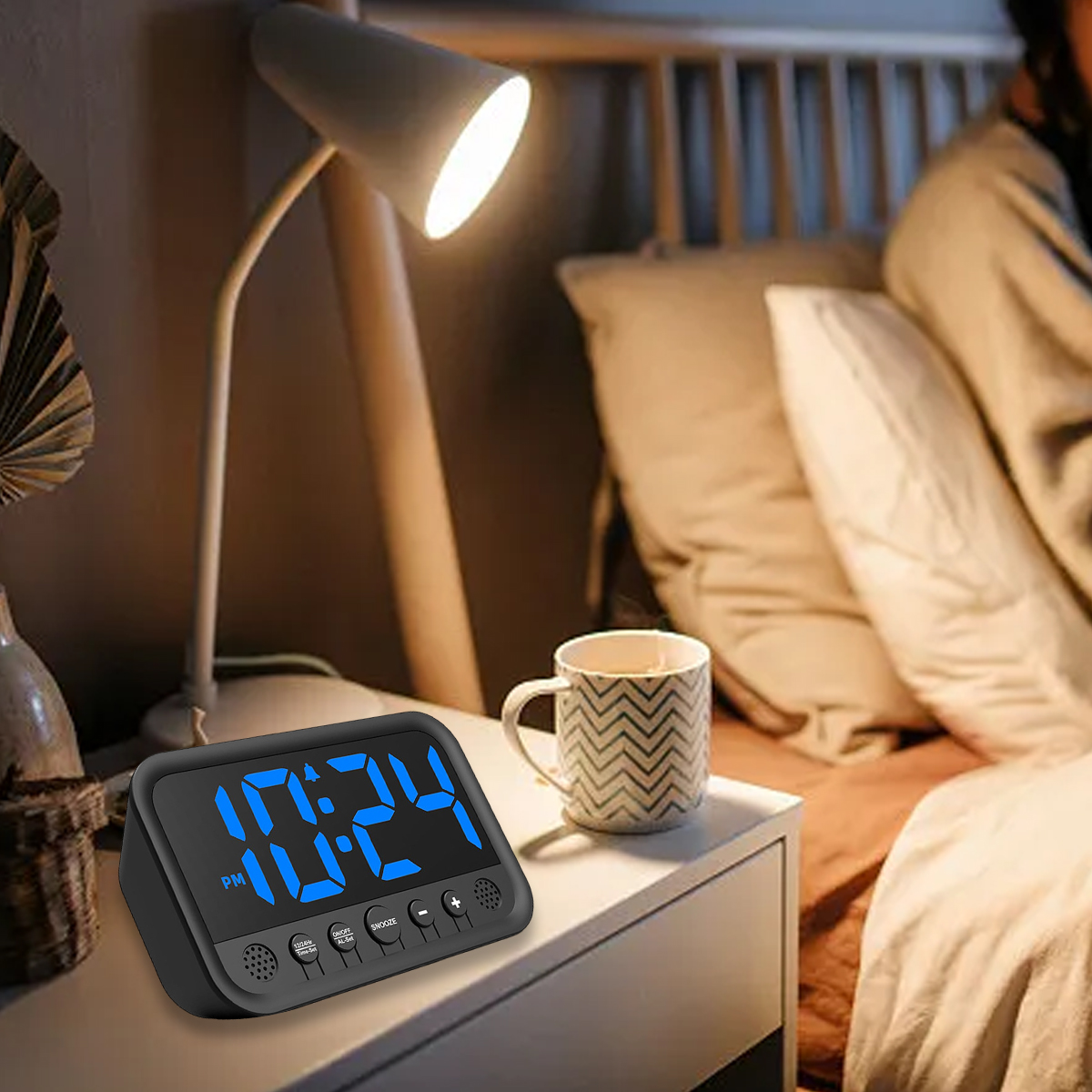 Ein digitaler Wecker mit blauen Zahlen steht neben einer Tasse und einer Lampe auf einem Nachttisch.